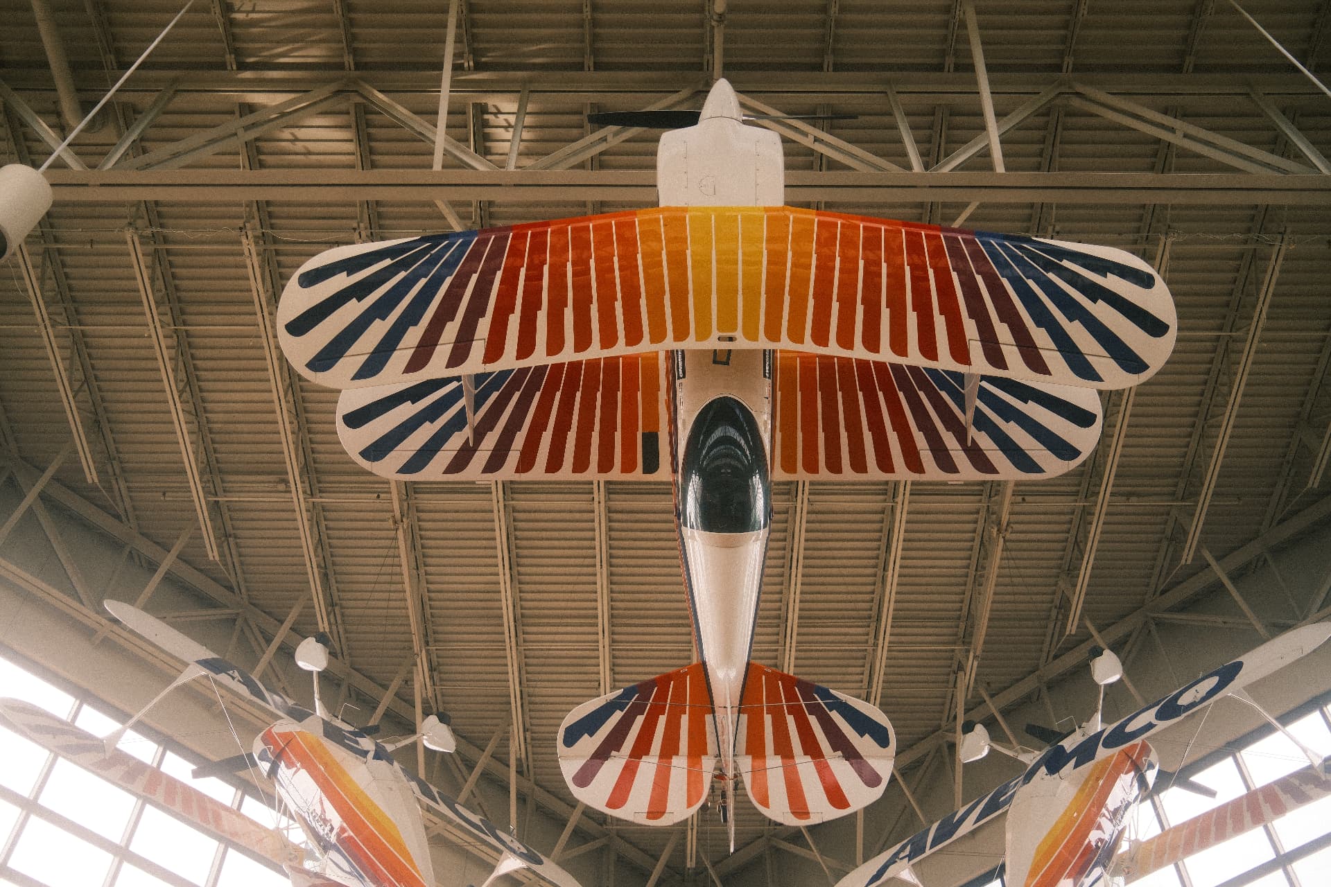 Colourful vintage aircraft suspended in a hangar, symmetrical view from below.